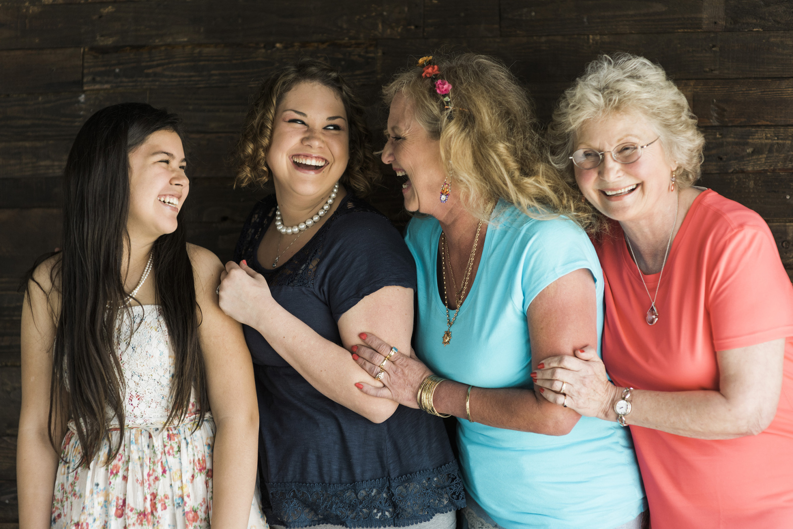 A four-generation family smiles at each other. Photo by Michelle Kirkland Photography.